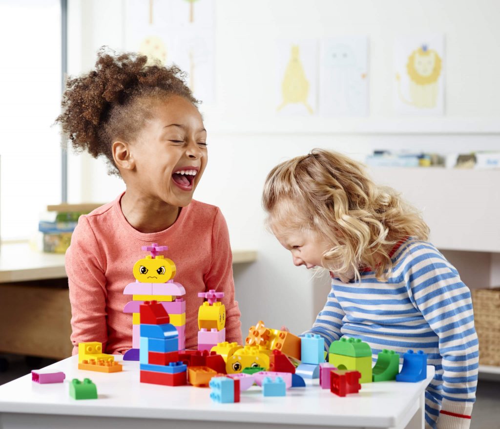 A imagem mostra duas crianças felizes brincando com lego.